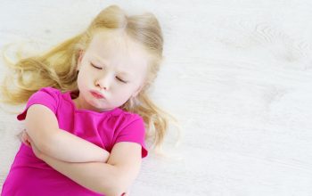 Very angry little girl lying on white wooden floor